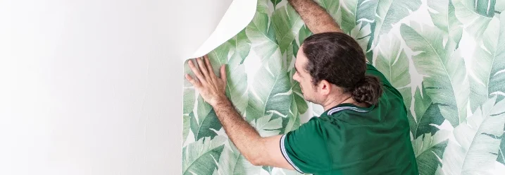 Person bringt Tapete mit Blättern an